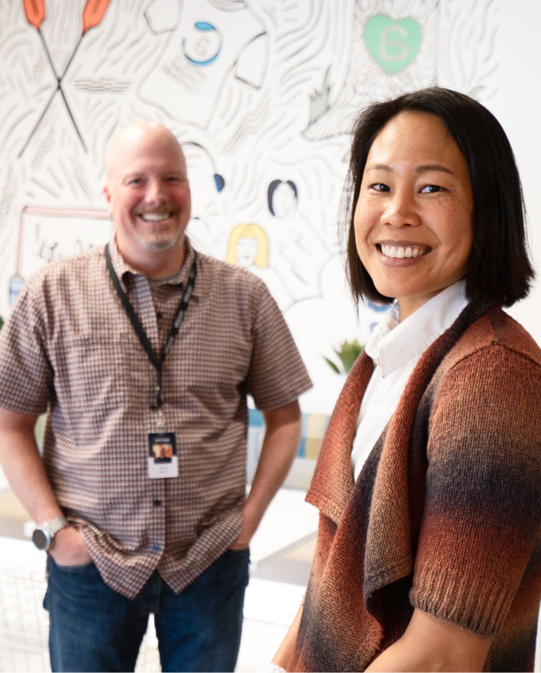 2 AppFolio employees in front of a cartoon wall background of an office. 