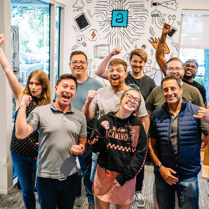 A group of various AppFolio employees in an office space, raising arms/fists in celebration.