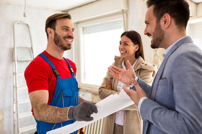 Contractor talking about details of home renovations to young smiling couple