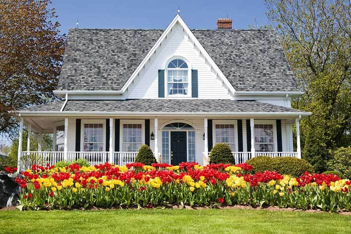 White farmhouse-style home with colorful flowers in front