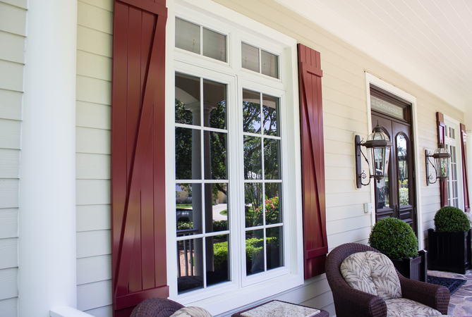 Red board and batten Colonial Shutters on an ivory-colored house's porch