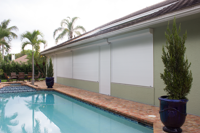 Closed White Roll Shutters covering windows and entry doors of a pool house