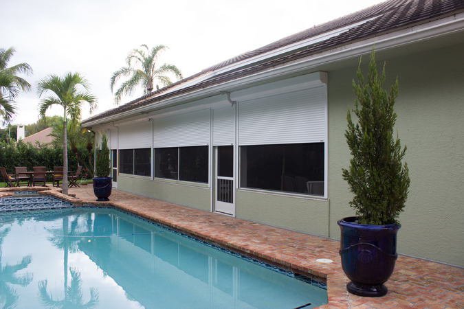 Half-open white Roll Shutters covering windows and entry doors of a pool house