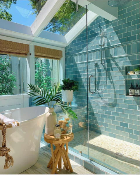 A nature-inspired bathroom with large windows, green tile, and many plants