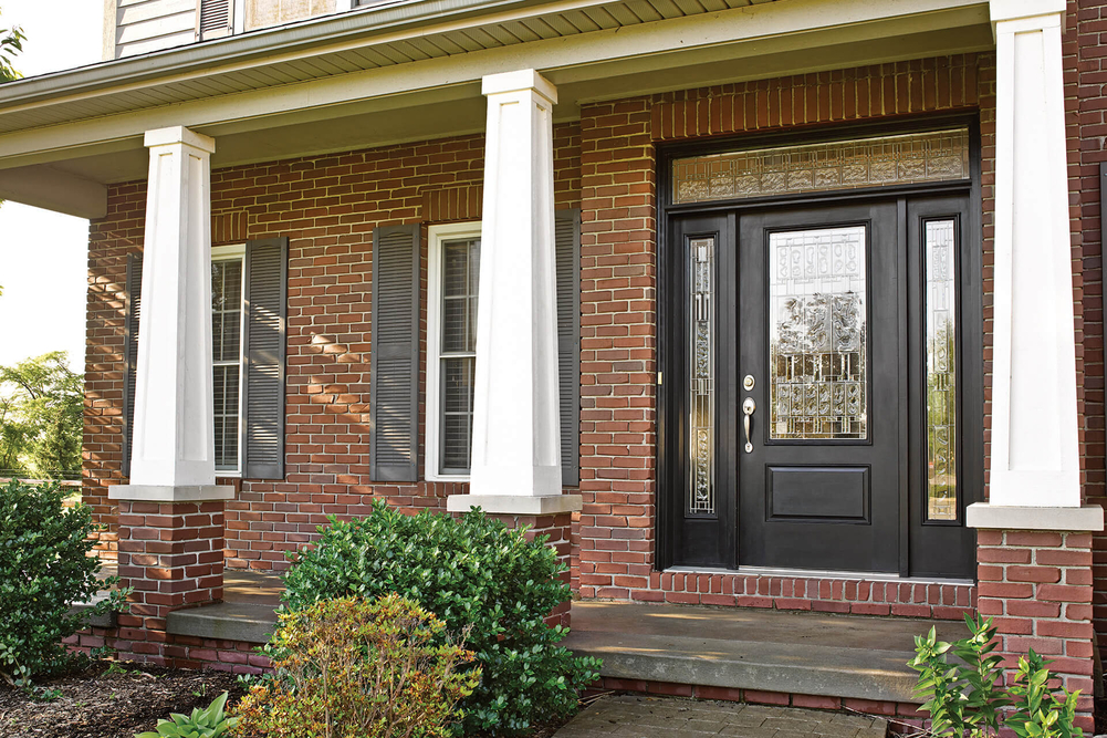 A brick home with columns and an exterior door features decorative glass