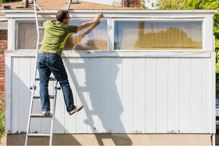 A man dangerously painting his house from a ladder