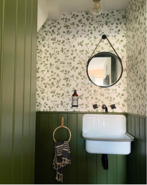 A unique green bathroom with stylish wallpaper and a circular mirror