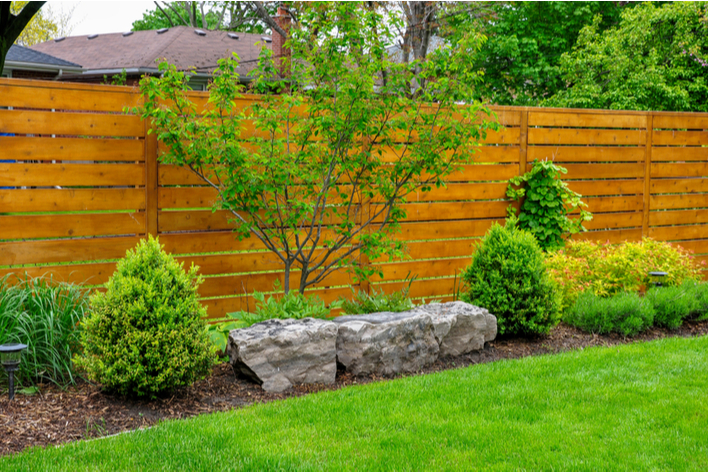 Fencing with horizontal lines, trees, and other landscaping features is used to update the exterior of a ranch-style house