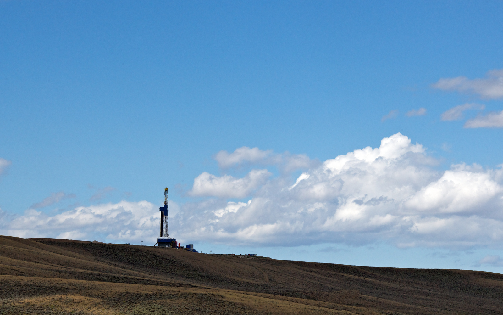 Oil rig in a field with a blue sky and clouds