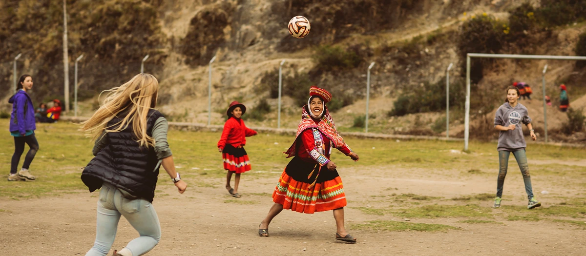 Students playing football with children in traditional Andean dress on a Peru immersion tour.