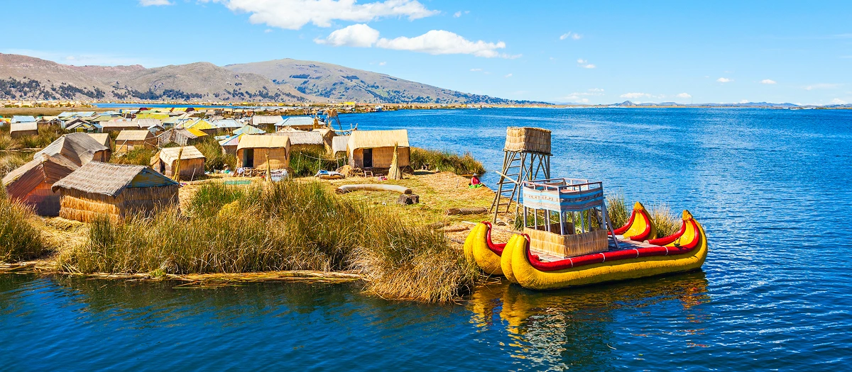 Floating reed islands and a traditional boat on Lake Titicaca in Peru on a sustainability tour.