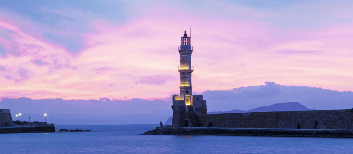 Historic stone lighthouse against a pink dusk sky, seen on Rome and Greece student tours.
