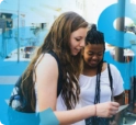 Two students on a class trip use a smartphone to manage their money