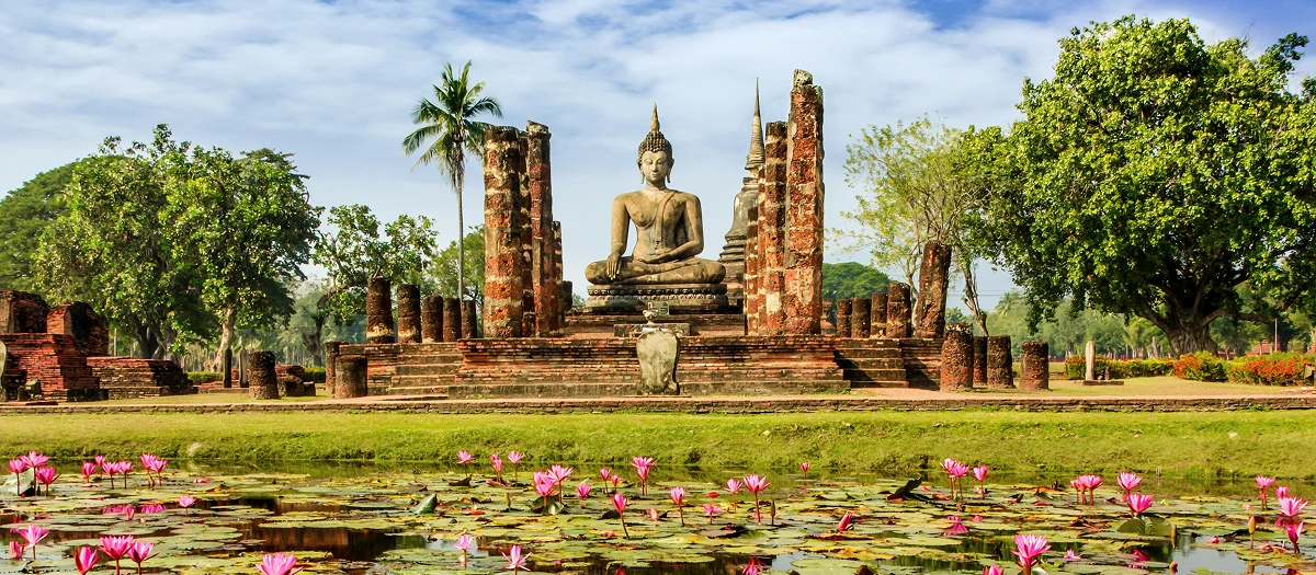 Seated Buddha among temple ruins and lotus flowers on the Treasures of Thailand tour.