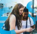 Two students on a class trip use a smartphone to manage their money