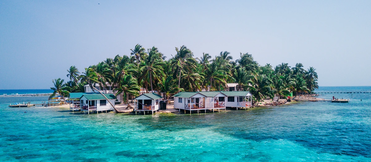 Palm island with stilt cabins in turquoise Caribbean water on a STEM conservation tour in Belize.
