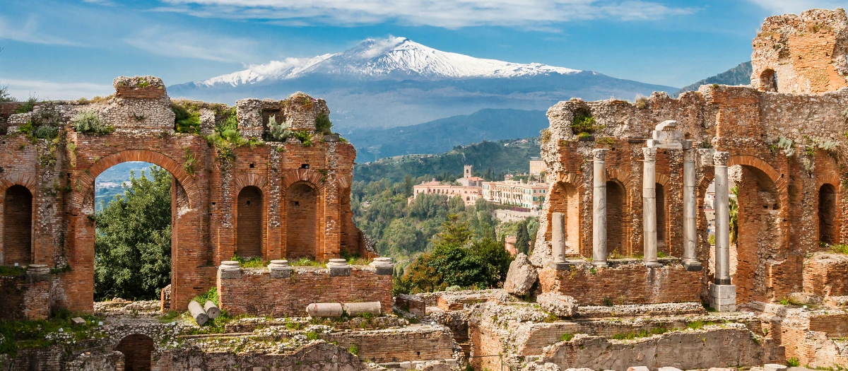 Ancient theatre ruins framing a snow-capped volcano in Sicily on a Rome to Sicily student tour.