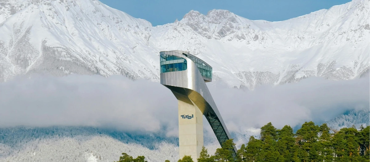 Modern ski jump tower above snow-covered Alps, seen on Germany and Italy student tours.