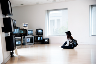 Girl sitting on floor, looking at multiple televisions