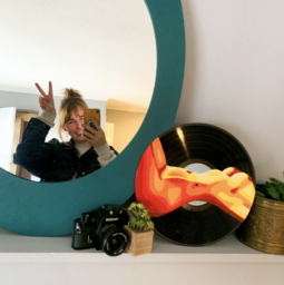 Artist Maggie Phipps poses in the mirror with one of her pieces