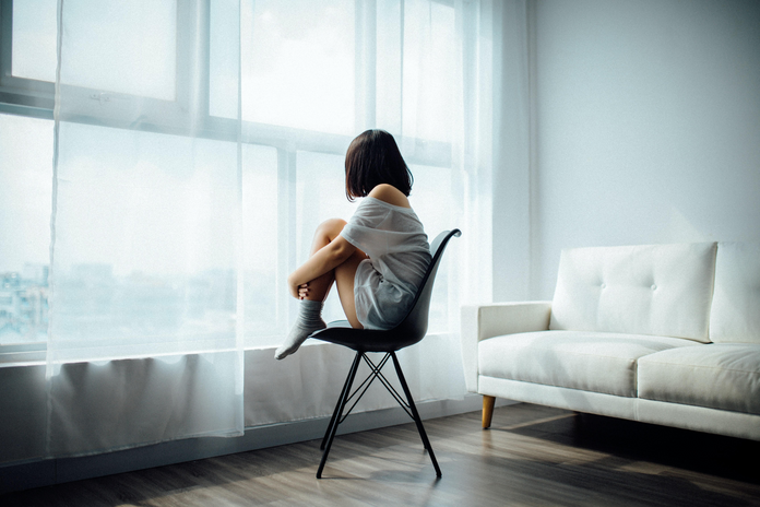 girl in white shirt sitting on a chair looking out the window
