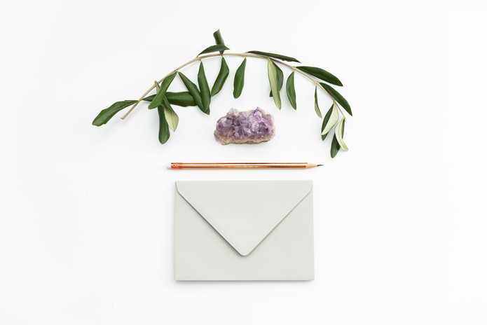 envelope, pencil, crystal, and plant on top of white surface