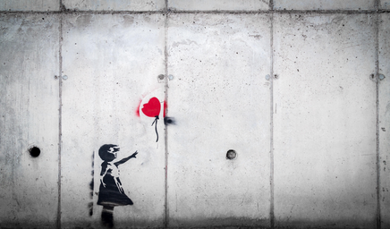 Spray painted on a grey wall - a little girl wearing a dress reaches for a red balloon.