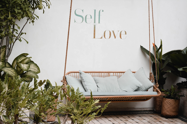 A swing in front of a spa in Bali that says self-love on the wall behind it