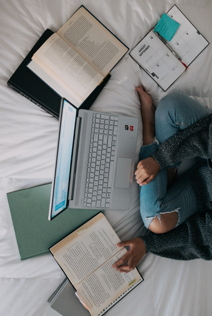 Woman in bed surrounded by laptop and books