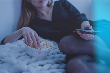 woman laying on side with remote eating popcorn