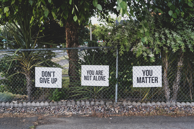 you are not alone signs along a metal fence