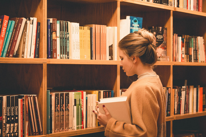 woman holding a book in front of a bookshelf