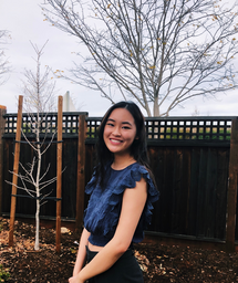 Girl in a blue top is smiling in front of a fence