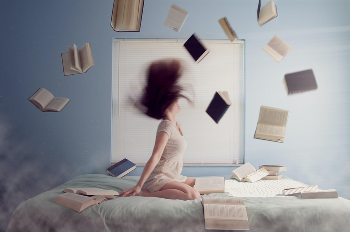woman sitting on bed surrounded by books by Lacie Slezak via Unsplash
