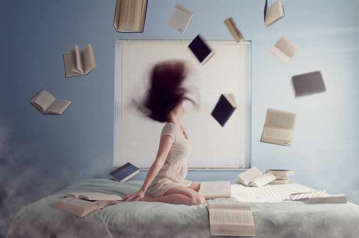 woman sitting on bed surrounded by books
