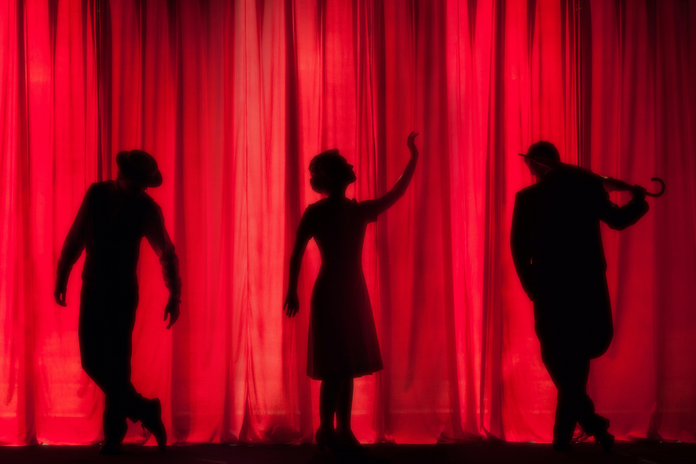 three figures in front of a red curtain