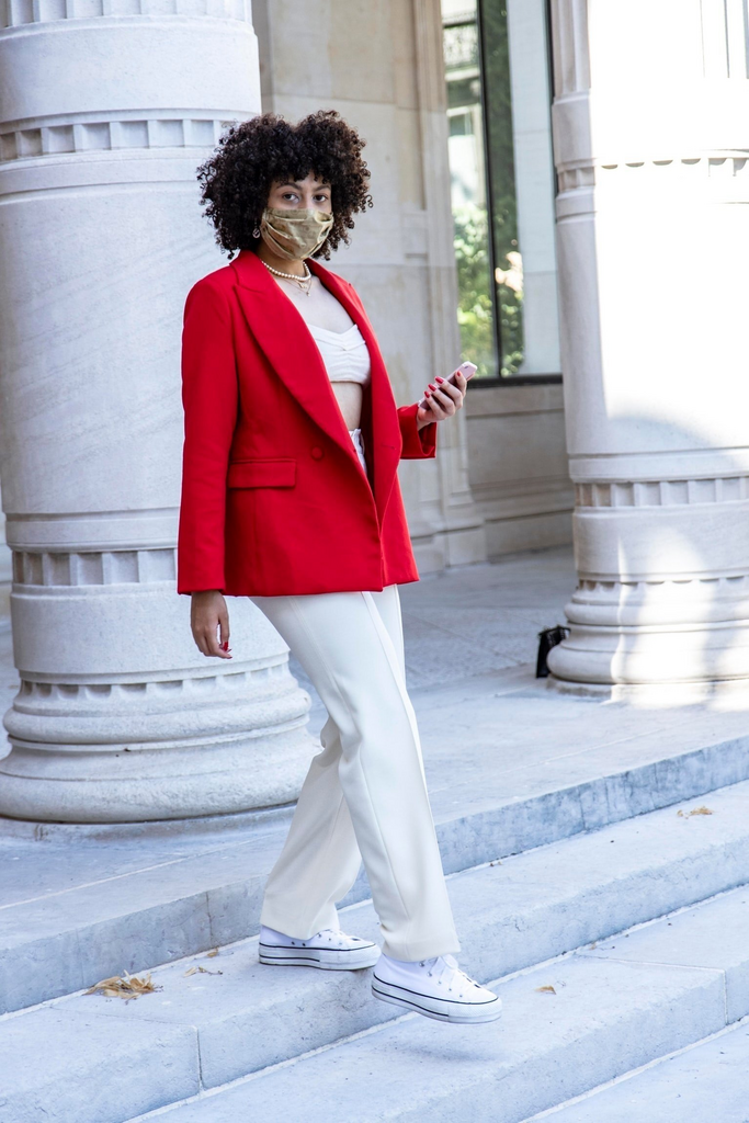 woman in red blazer and white pants with face mask walking down staircase