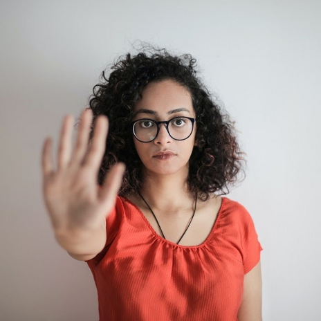 portrait photo of woman in red top wearing black framed eyeglasses holding out her hand stop gesture