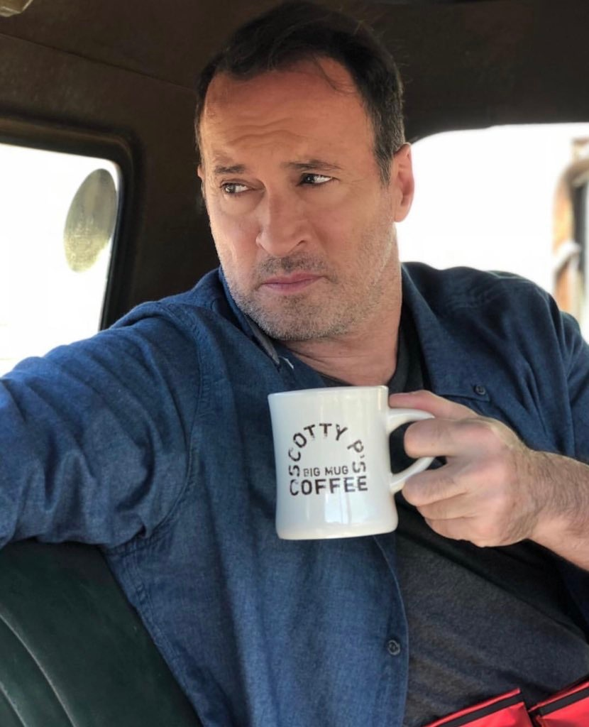 Image of Scott Patterson sitting in a car holding a cream-coloured coffee mug with the words \