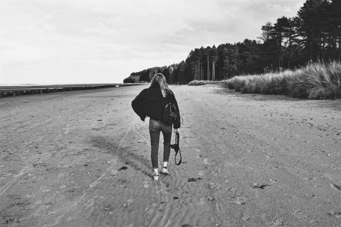 black and white photo of woman walking away on a beach