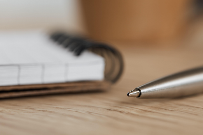 zoomed in picture of a pen and a notebook (blurry) in the background