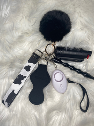 Self defense keychain with a pepper spray, led light/panic button, self defense tool, lip gloss holder, pom pom, and cow printed wristlted is displayed against a white fluffy background