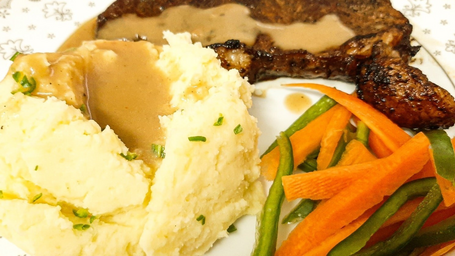 mashed potatoes with gravy, carrots and peppers, and steak on plate