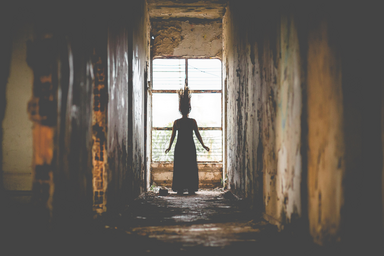 Woman in a dilapidated corridor looking out a window