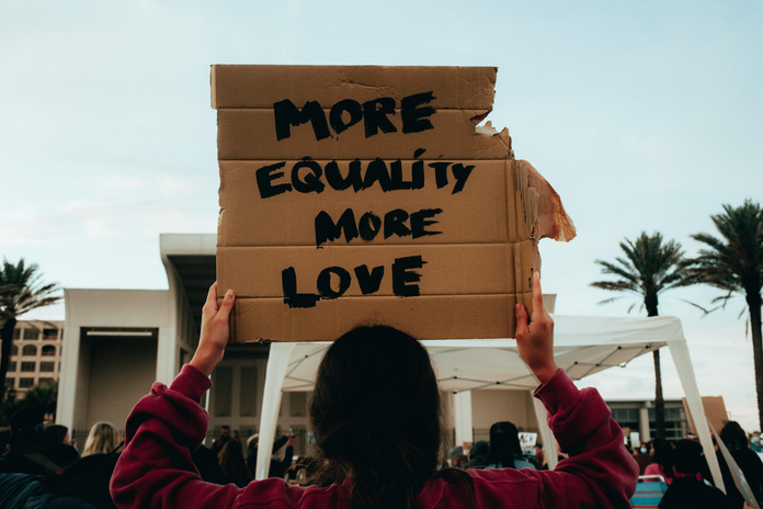Person holding cardboard sign saying \"more equality, more love\"