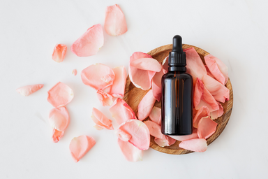 essential oil bottle sitting in a wooden bowl of rose petals