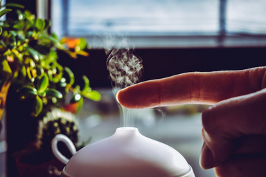A person putting their finger in the mist from a diffuser.
