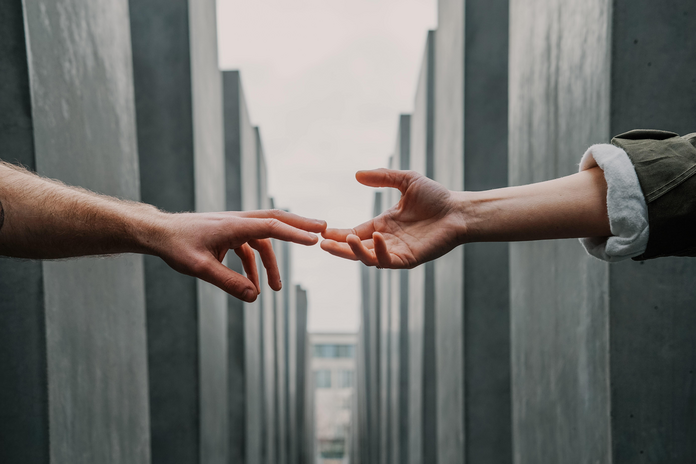 Two hands reaching for each other against a grey background.