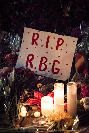 A poster saying R.I.P R.G.B laying on flowers and candles at Ruth Bader Ginsberg\'s memorial.