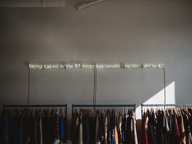 racks of clothing against a wall with a slogan written above them